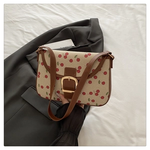 Détail du sac bandoulière en toile à imprimé cerises, bordure cuir marron et boucle métal