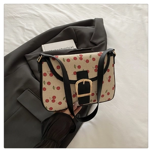 Détail du sac à bandoulière imprimé cerise avec fermoir doré sur un blazer gris chic