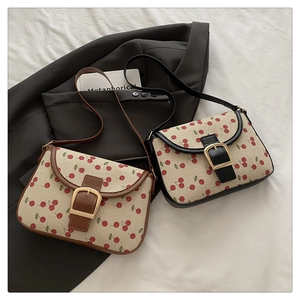 Détail de sacs bandoulière en toile avec motif cerise, bords en cuir et boucles dorées