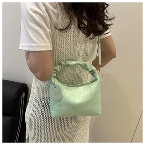 Gros plan d'un sac à main plissé vert clair avec texture et pendentif de mode rond