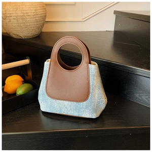 Detail of denim tote bag with gold studs and brown leather handles on dark stairs