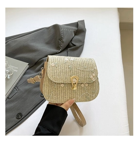 Détail d'un sac en paille tressée avec broderie florale et fermoir rotatif doré