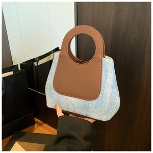 Detail of blue denim tote bag with brown leather circular handle and metal rivet base