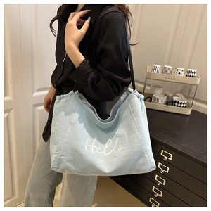Detail of light blue denim tote bag with white Hello embroidery in a home setting