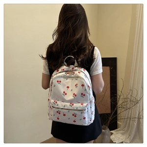 Rear view of model wearing a white backpack with red cherry patterns and zip pockets