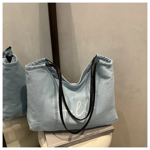 Close-up of light blue denim tote bag with white Hello embroidery and black leather straps