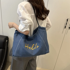 Blue denim tote bag with yellow Hello embroidery and black leather straps on model