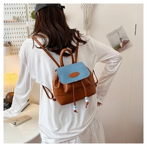 Detailed back view of a mini brown leather and blue denim backpack on a female model