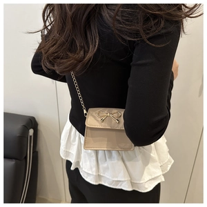 Detail of beige mini crossbody bag featuring a gold bow buckle and fine chain strap