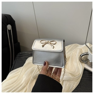 Detail showing a silver mini square bag with golden bow buckle and chain strap