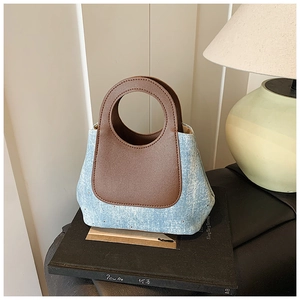 Detailed shot of a denim bucket bag with brown leather handles on books