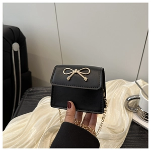 Close-up of black mini crossbody bag featuring a golden bow buckle and fine chain strap