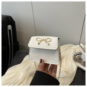 Detail of a creamy white mini chain bag featuring a gold bow buckle and leather texture