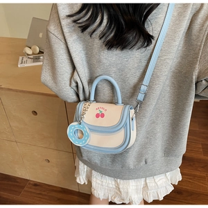 Detail of saddle bag with cherry pattern and donut charm on a grey sweatshirt