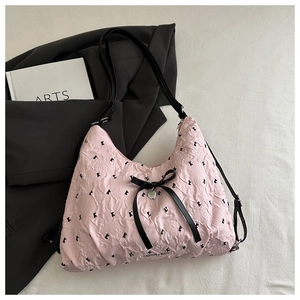 Detailed view of pink crinkle fabric shoulder bag with black bows and metal heart pendant