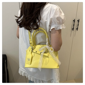 Detail view of yellow crossbody bag with delicate white lace bow on matte faux leather