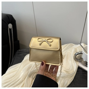 Detailed view of mini gold handbag with bow clasp and elegant chain held in hand