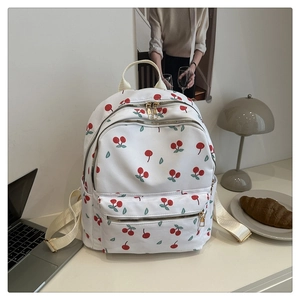 Detail of white canvas backpack with cherry print and golden zippers on a desktop