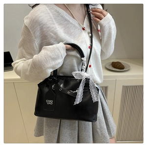 Detail of a black leather square bag featuring a large white lace bow and a branded tag