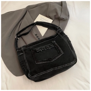 Dettaglio borsa in denim nero con cuciture a contrasto bianche e texture con frange