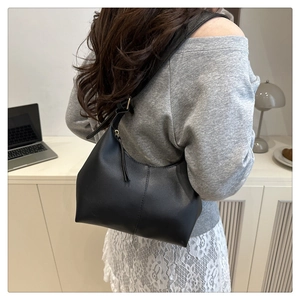 Detail of a black leather hobo bucket bag worn as a shoulder bag in a modern office setting