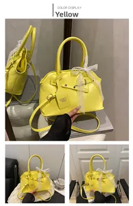 Detail of yellow leather handbag featuring lace bow decoration and branded tag charms