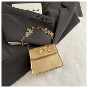 Detail of a mini gold crossbody bag with a metallic bow and fine chain strap