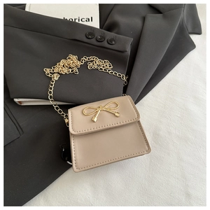Mini beige crossbody bag with gold bow clasp and chain strap on stylish background