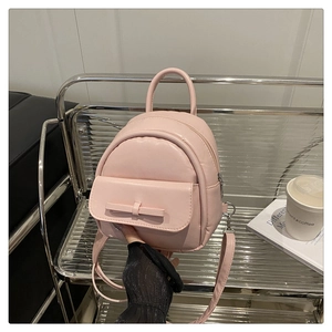 Pink mini faux leather backpack with bow detail shown on a stylish display shelf