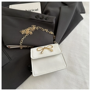Close-up of a white leather mini flap bag featuring a gold metal bow and chain strap