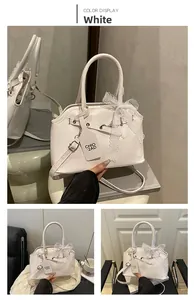 Detailed shot of white leather shell bag featuring lace bow and metallic buckle accent