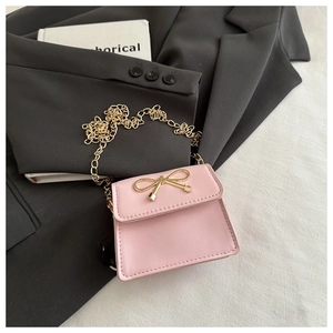 Detail shot of a pink mini crossbody bag with a golden metal bow on a grey blazer