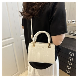 Detail of cream white textured handbag with woven handles and golden hardware accents