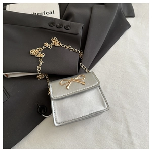 Detail of silver mini crossbody bag with golden bow buckle on black blazer jacket