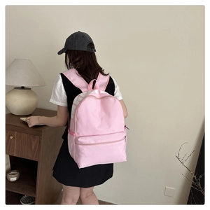 Pink nylon backpack detail showing front zipper pocket and white letter print for students