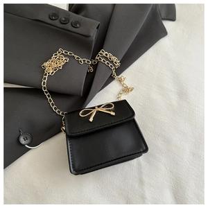 Detail of a mini black crossbody bag featuring a gold bow buckle and elegant metal chain