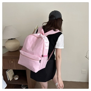 Pink nylon student backpack with side mesh pocket shown in a cozy dorm room setting
