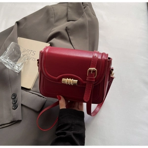 Close-up of dark red crossbody bag with gold cylindrical metal lock and smooth stitching