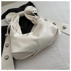 Detail of cream faux leather handbag featuring oversized bow and silver studded rivets