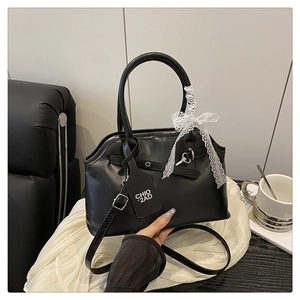 Detail of black leather handbag featuring white lace bow and adjustable crossbody strap