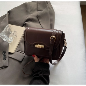 Detail of a coffee brown crossbody square bag with gold metal buckle on a grey blazer