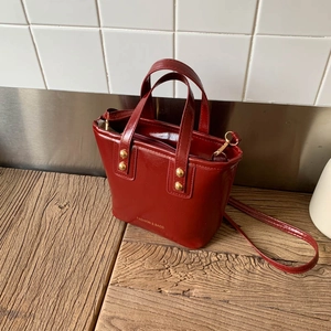 Detailed top view of a shiny burgundy bucket bag with gold studs and top zipper closure