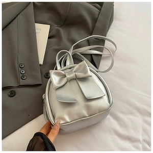 Close-up of a stylish silver mini backpack featuring a large decorative bow and thin straps