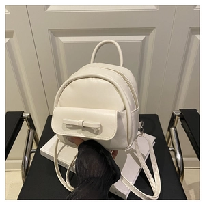 Detail of a creamy white mini backpack featuring a bow-knot front pocket on a chair