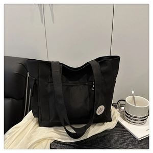 Detail of black canvas tote bag showing side flap pocket and good luck badge