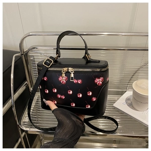 Detail of a black box bag with cherry print, golden double zippers and adjustable strap