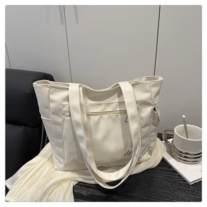 Detail of cream tote bag front zipper pocket and decorative 'good luck' patch on desk