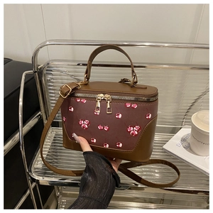 Close-up of retro box bag with cherry print and golden zippers held by a hand