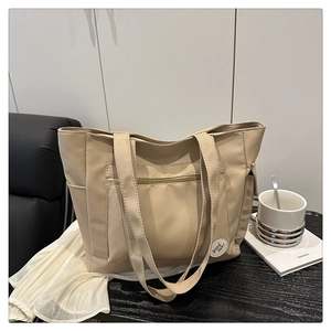 Detail view of beige canvas tote bag with front zipper pocket and decorative logo tag