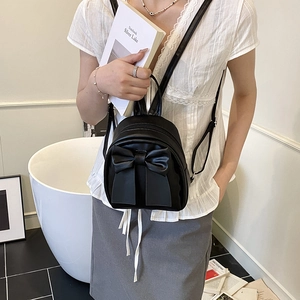 Chic black mini backpack with oversized bow detail worn by model in a minimalist room
